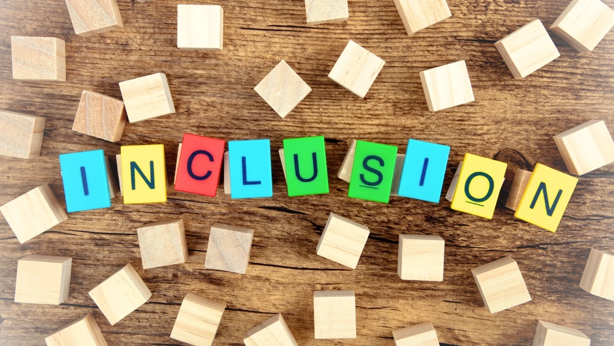 Blocs de bois colorés formant le mot "INCLUSION" sur un fond en bois rustique, illustrant la diversité des profils DISC et l'inclusion comportementale en entreprise.